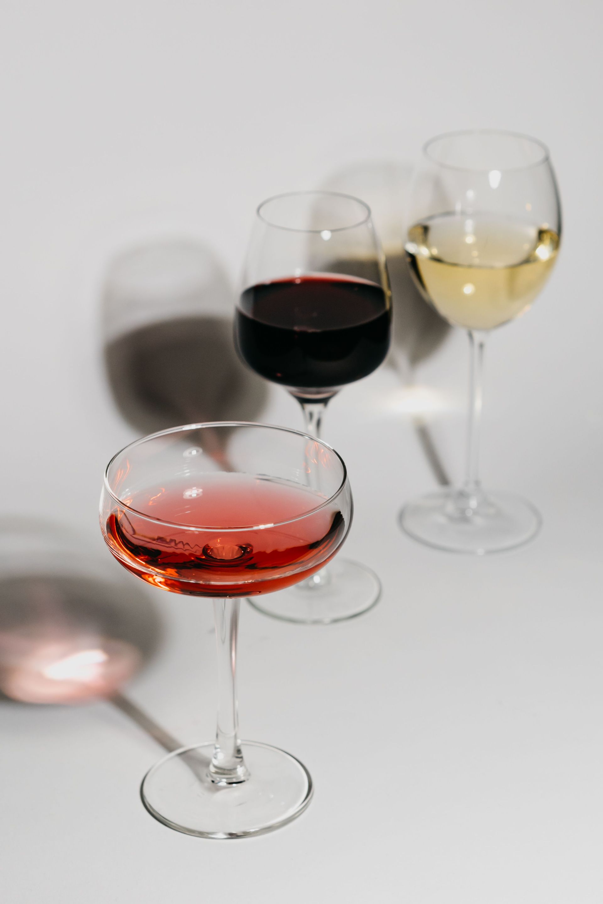 Three wine glasses with red, white, and rosé wines casting shadows on a white background.